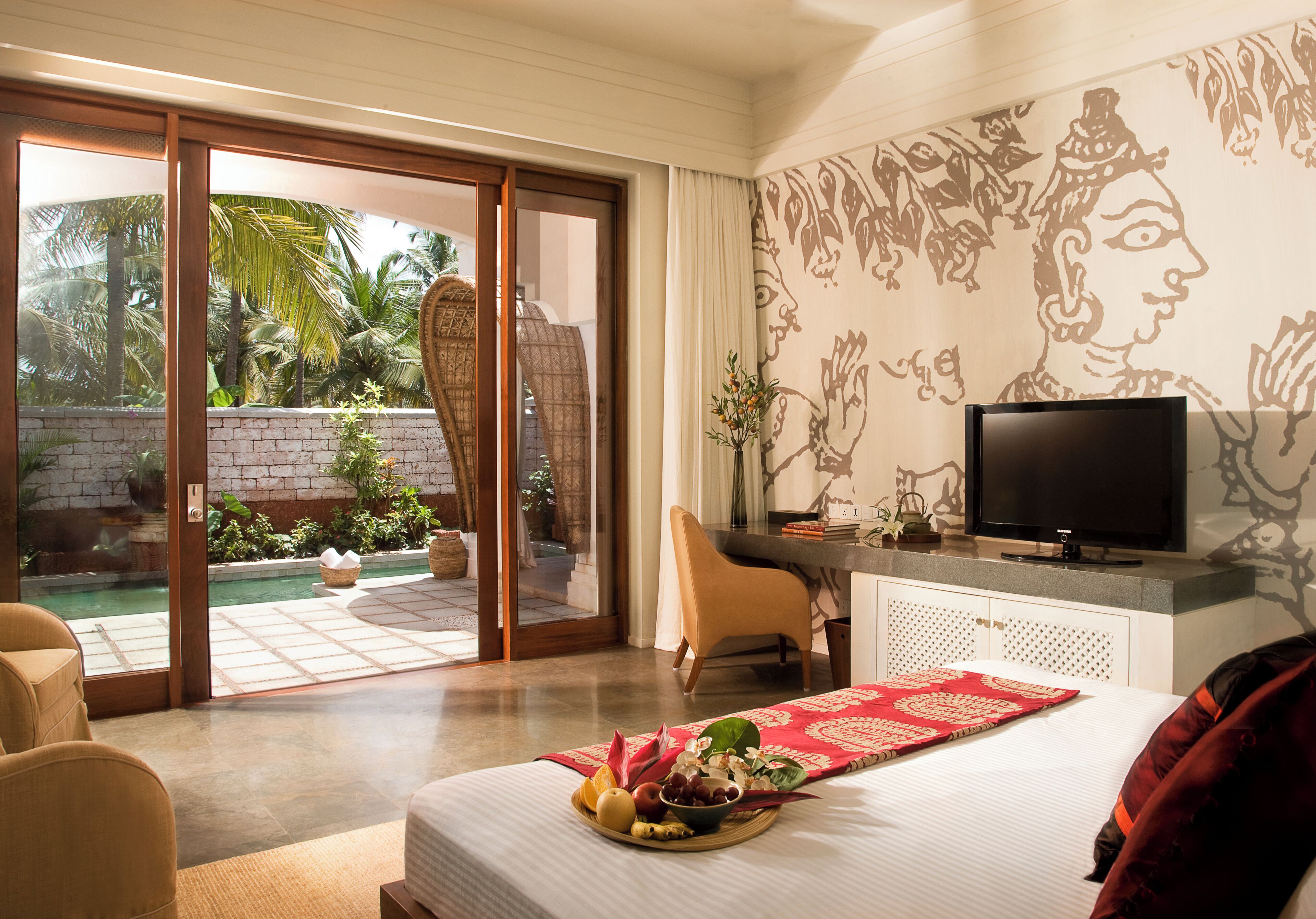 A hotel room with a bed, a television, a desk, and a view of a pool and palm trees.