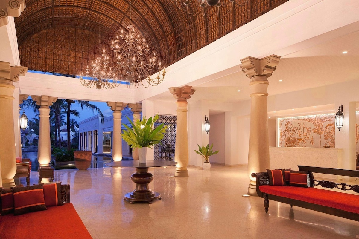 A spacious lobby with high ceilings, ornate columns, and a grand chandelier.
