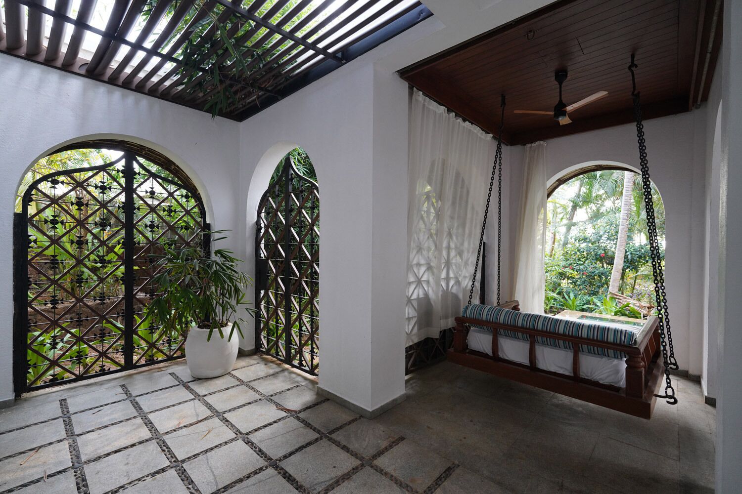 Una habitación con un banco de madera, una planta en maceta y vistas a través de una puerta celosía.