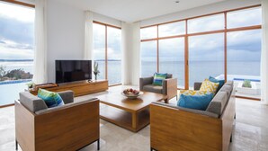Uma sala de estar moderna com uma televisão grande, assentos confortáveis e vista para o mar.