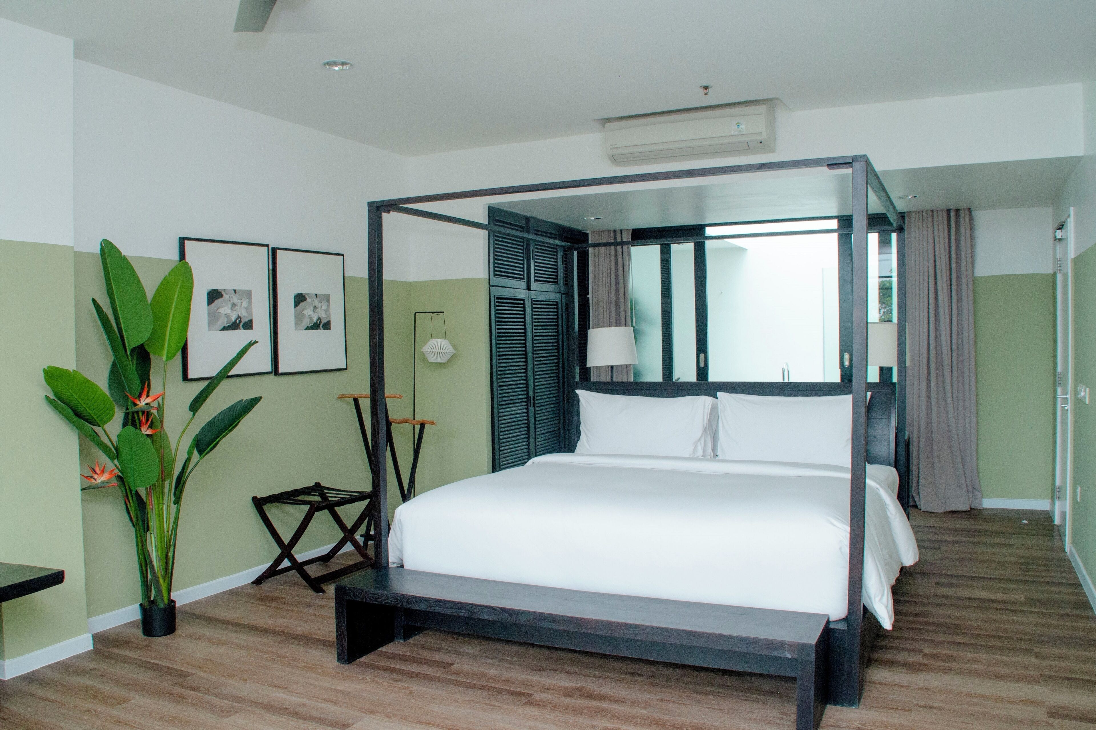 A four-poster bed with a canopy, a potted plant, and framed pictures on the wall.