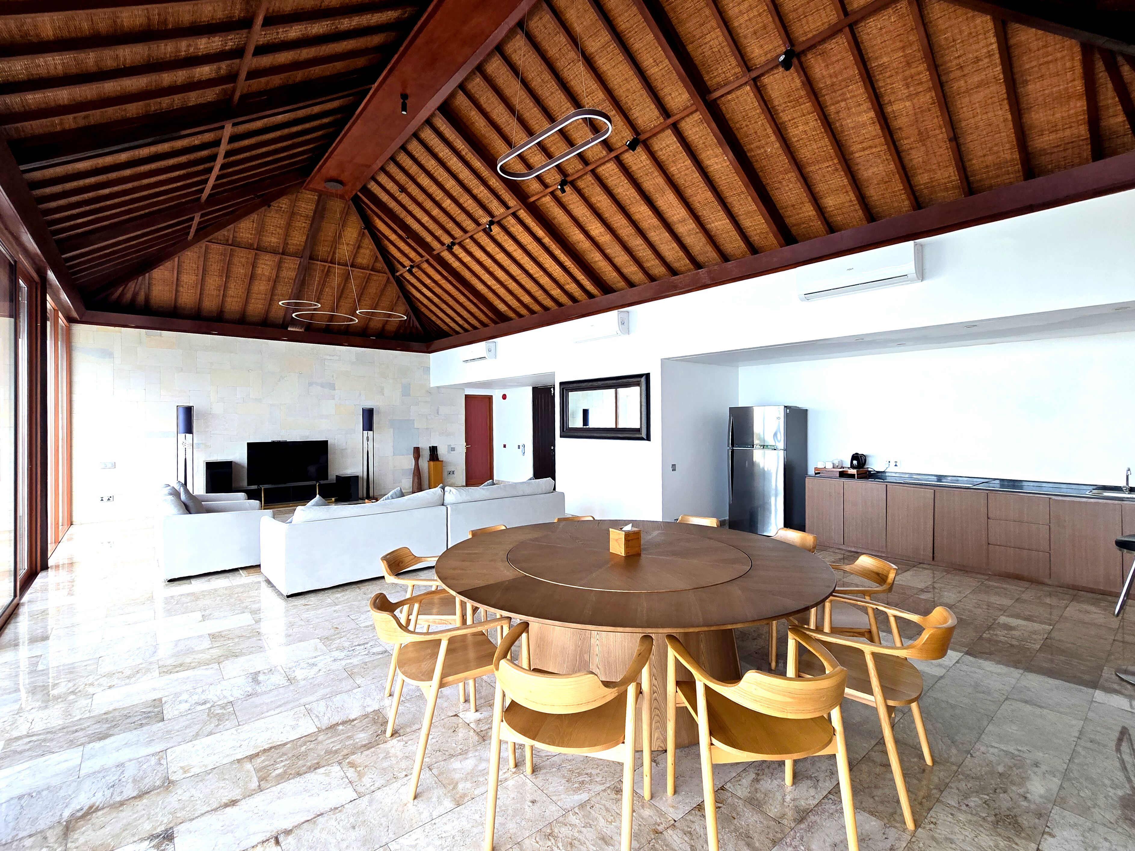 A spacious kitchen with a central island, a dining area with a round table and wooden chairs, and a modern living area with a sofa and flat-screen TV.