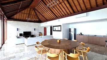 A spacious kitchen with a central island, a dining area with a round table and wooden chairs, and a modern living area with a sofa and flat-screen TV.
