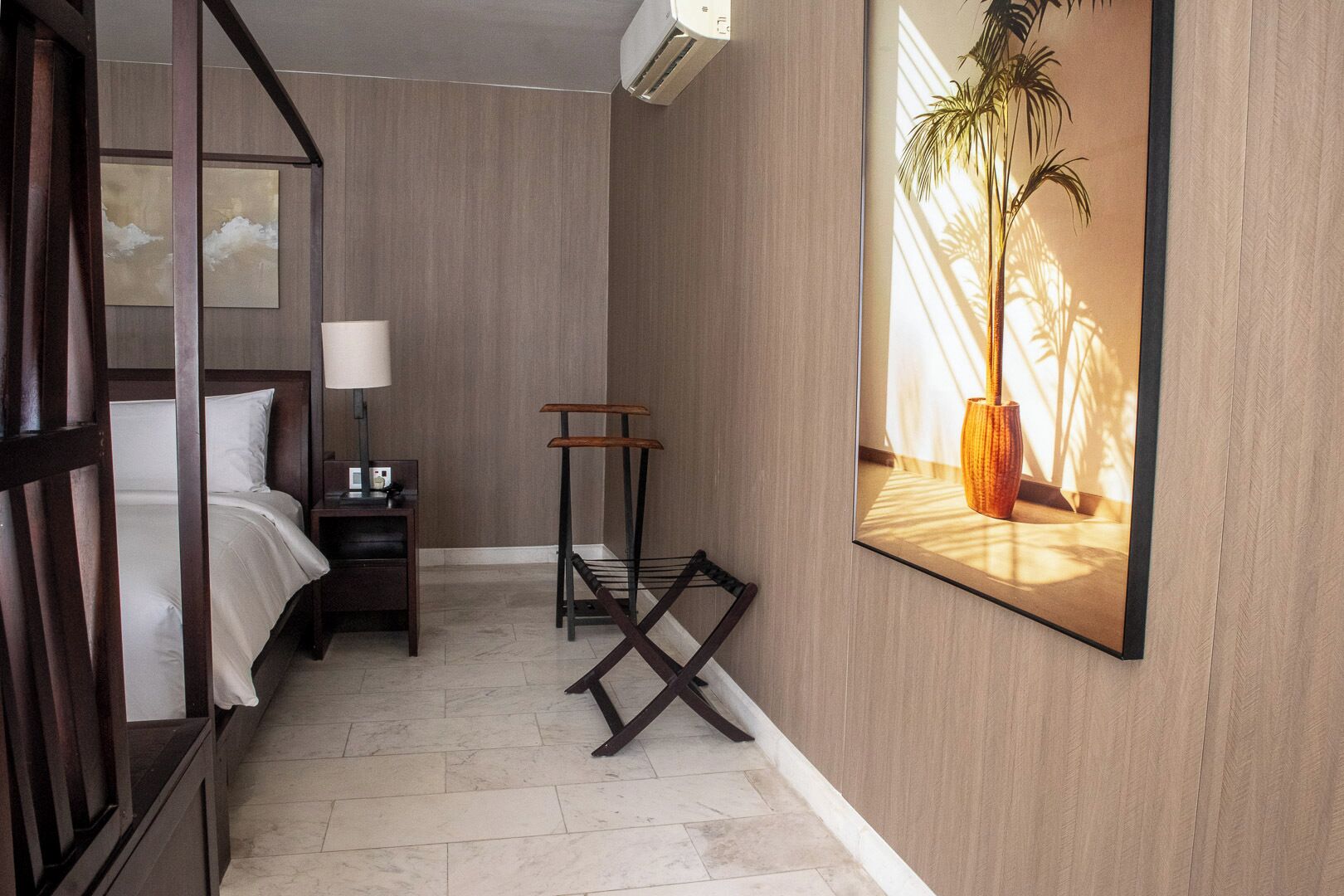 Een hotelkamer met een bed, nachtkastje, lamp en een lijst met een afbeelding van een plant.