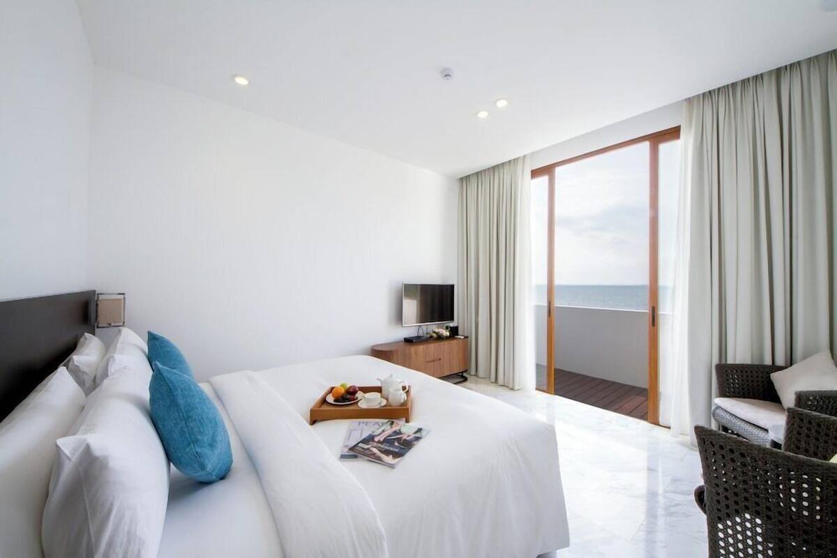 Ein Hotelzimmer mit Bett, Fernseher, einem Holztischchen, einer Ablage mit Früchten und einer Tasse sowie einem Balkon mit Blick.
