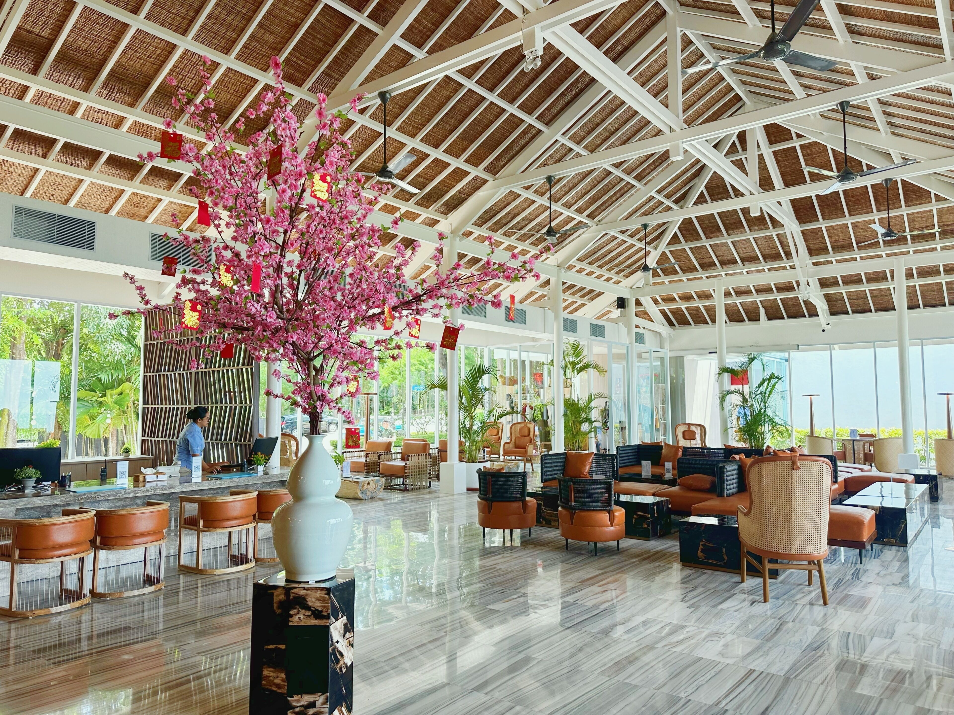 A spacious indoor area with a high ceiling, large windows, and a central decorative tree.