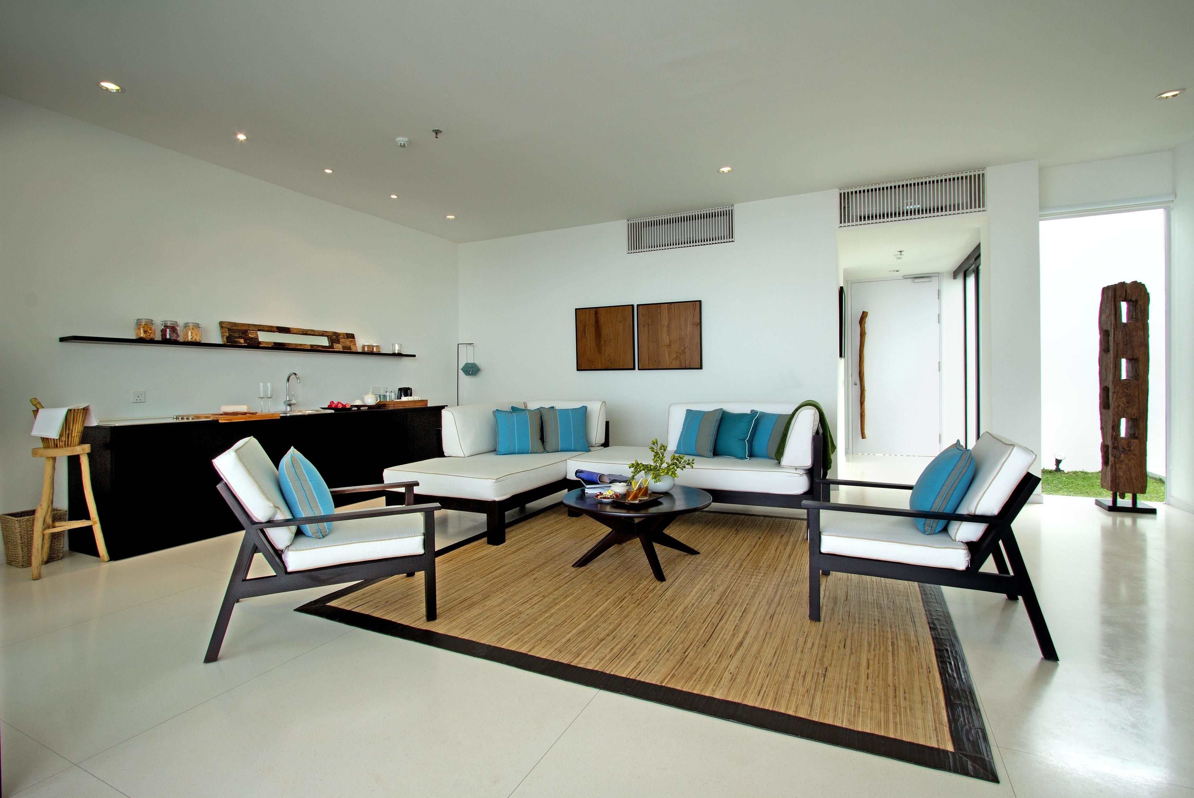 Una sala de estar moderna con un sofá modular, dos sillones, una mesa de centro y una zona de cocina con mostrador y estanterías.