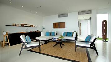 Una sala de estar moderna con un sofá modular, dos sillones, una mesa de centro y una zona de cocina con mostrador y estanterías.