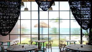 Um restaurante com grandes janelas, mesas e cadeiras de madeira.