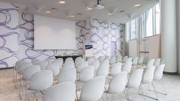 A conference room with rows of white chairs, a large white screen, and a projector.