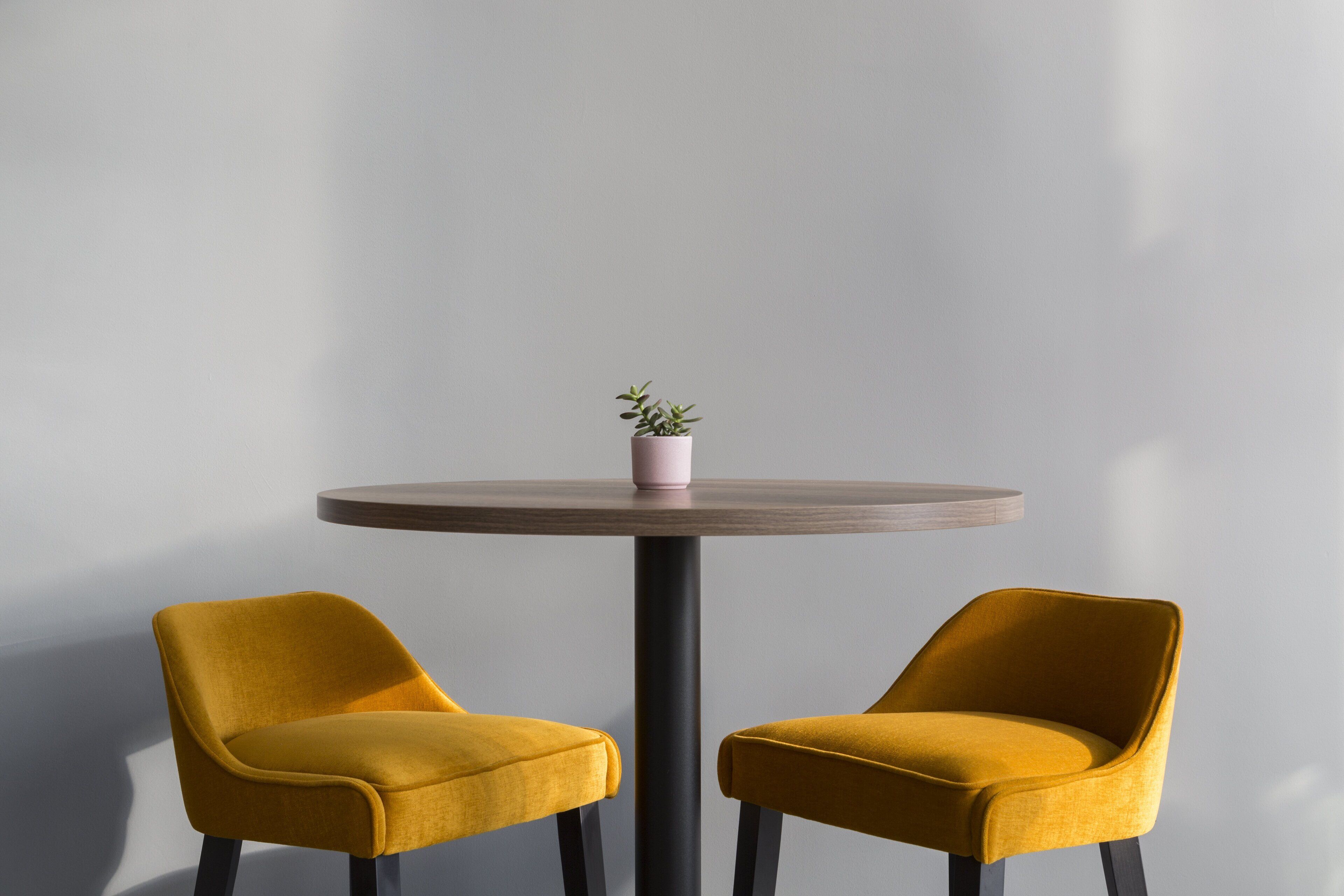 Two mustard-colored chairs around a round table with a small potted plant on top.