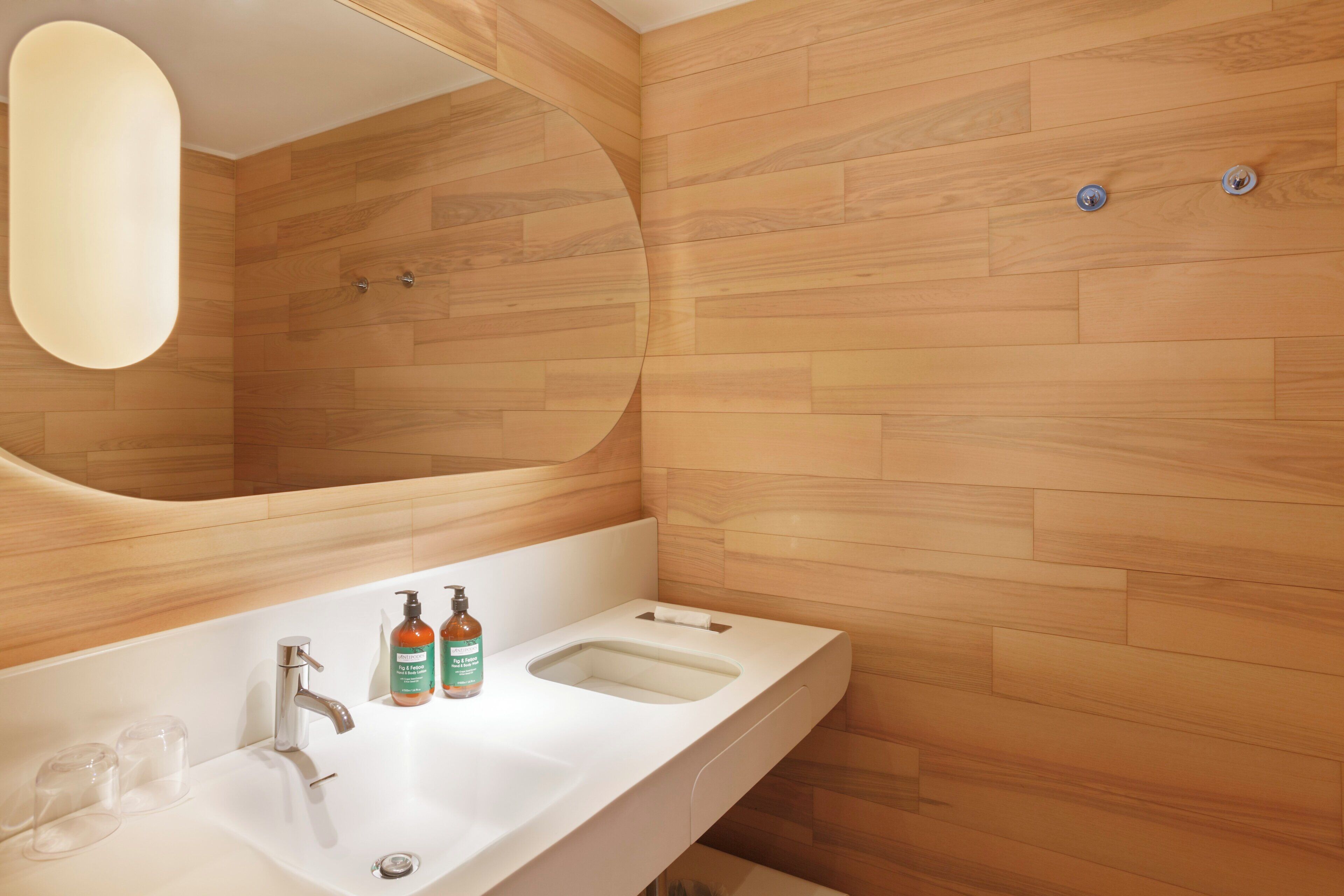A modern bathroom with a large mirror, two sinks, and wooden wall panels.