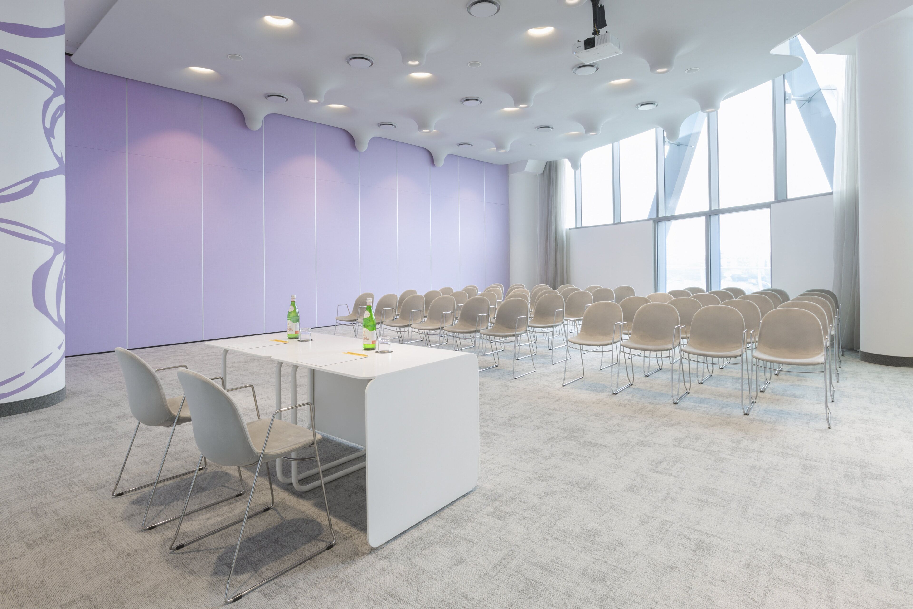 A conference room with a white table and chairs, large windows, and a purple wall.