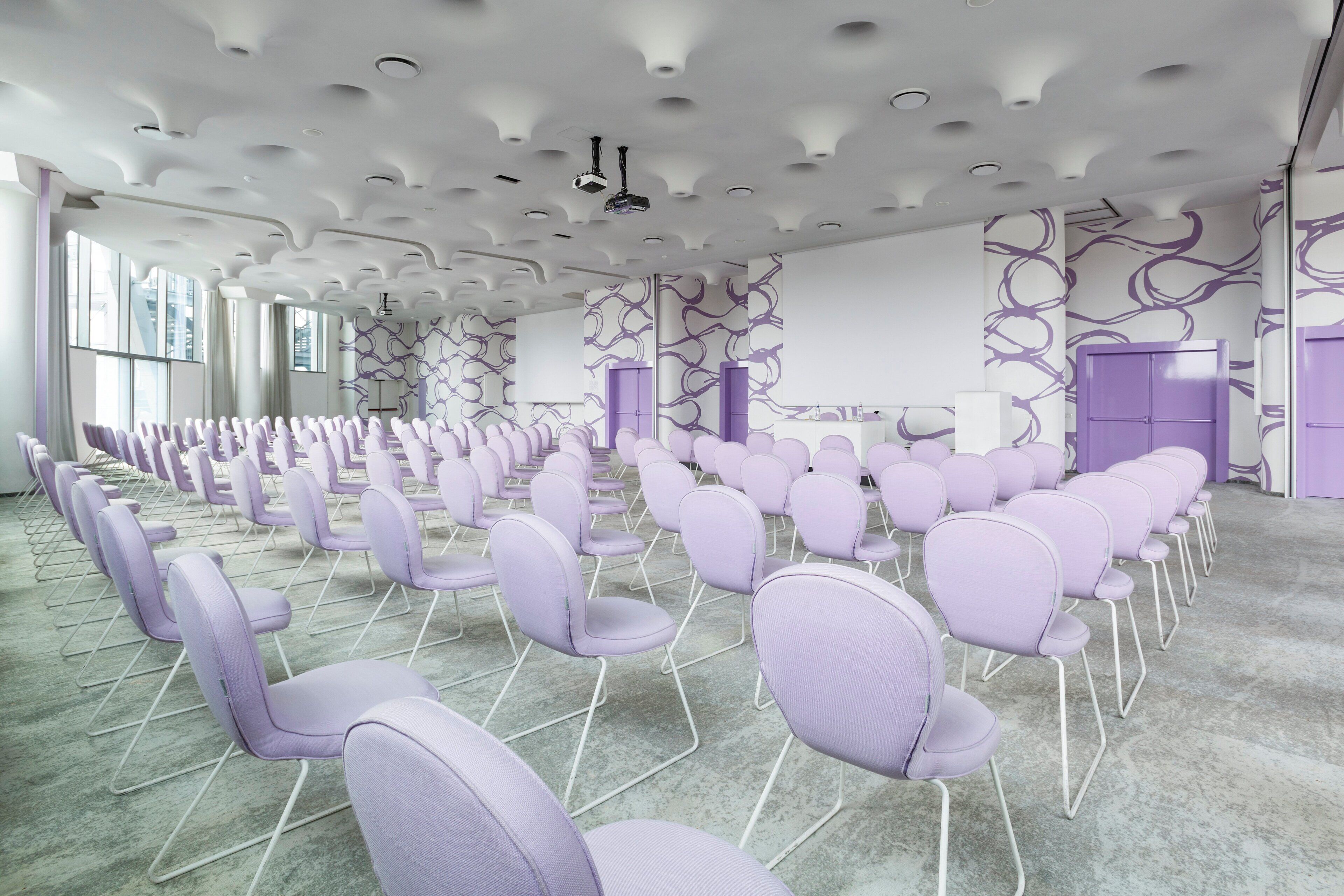 Een vergaderzaal met rijen stoelen, een beamer en een scherm.