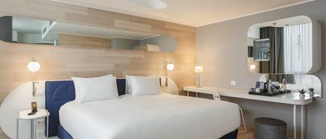 A modern hotel room with a large bed, bedside tables, a desk, and a mirror.