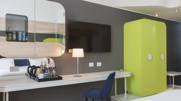 A modern hotel room with a white desk, a blue chair, a green wardrobe, a flat-screen TV, and a mirror reflecting the room's interior.