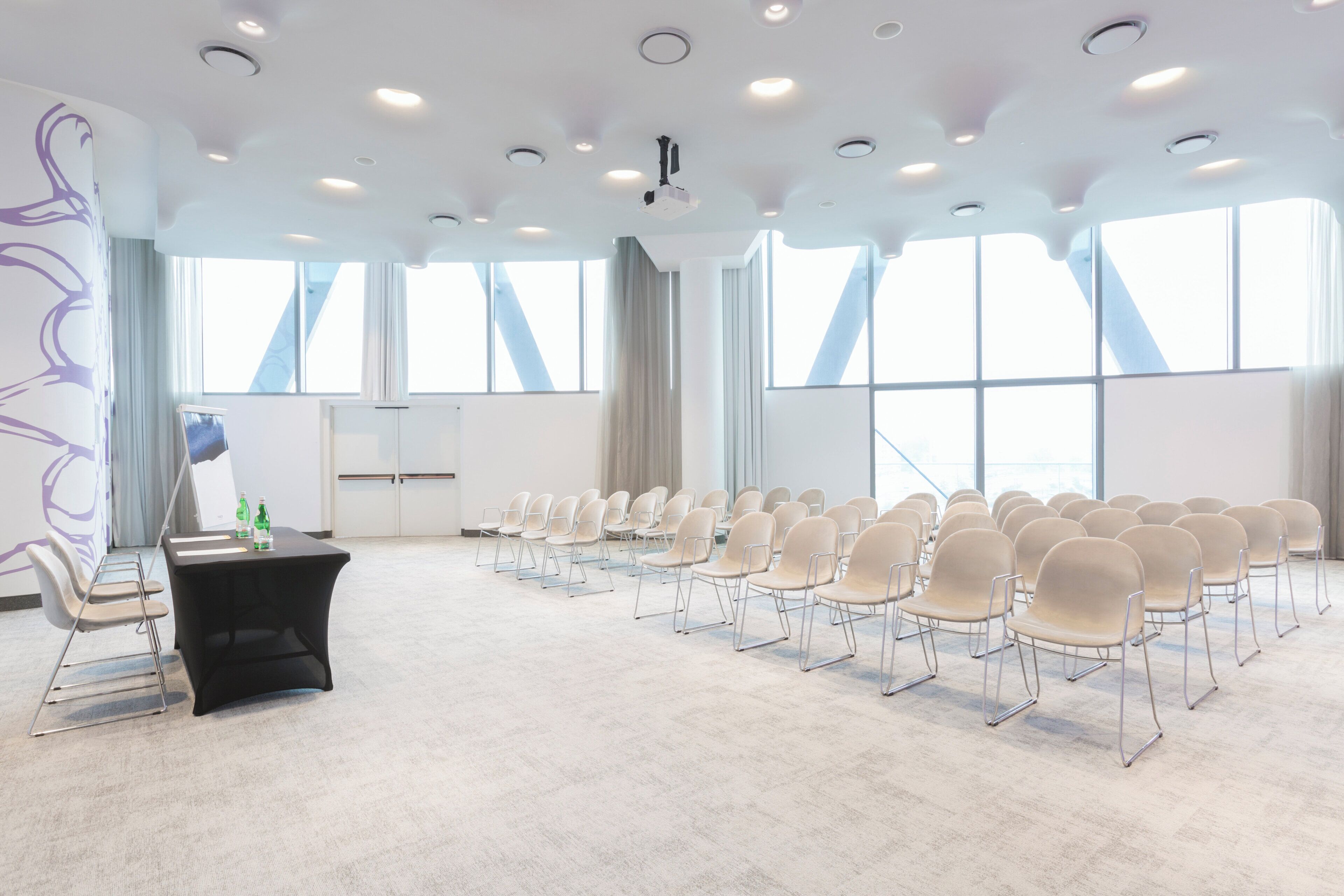 Un salón de conferencias con filas de sillas, un atril y ventanas amplias.