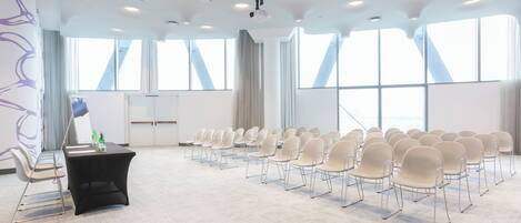 Un salón de conferencias con filas de sillas, un atril y ventanas amplias.