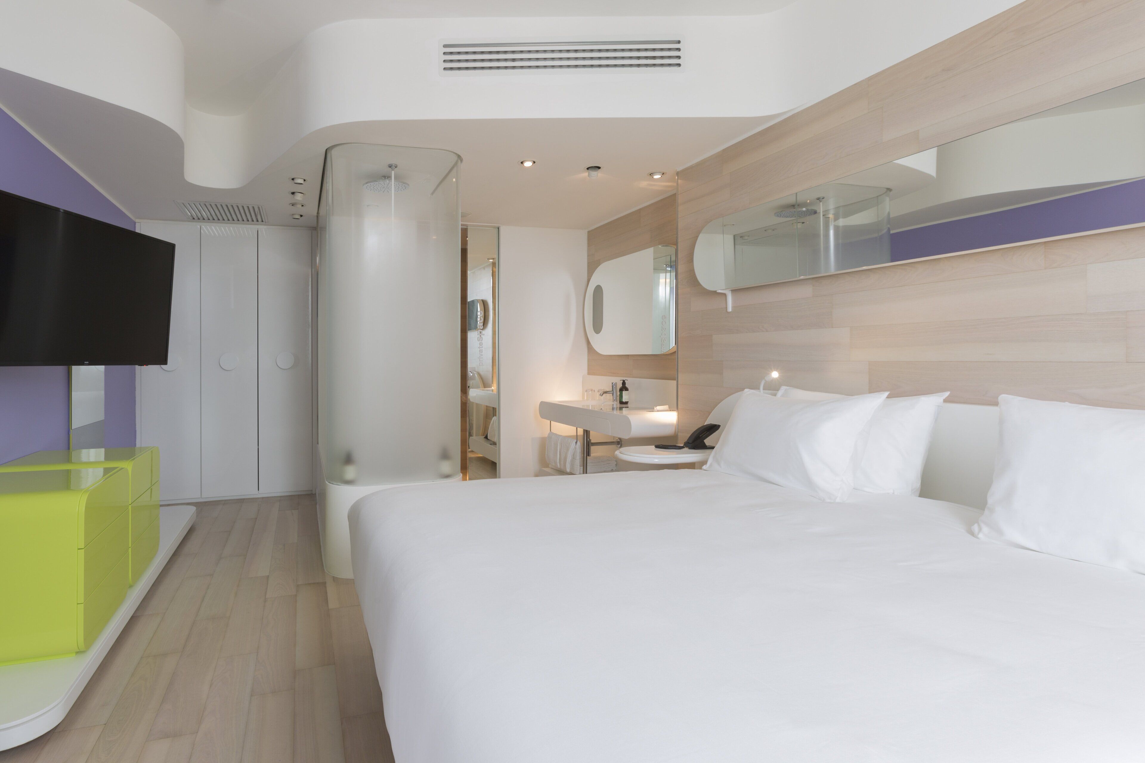 Une chambre d’hôtel moderne avec un grand lit, une salle de bain avec un miroir et un téléviseur fixé au mur.