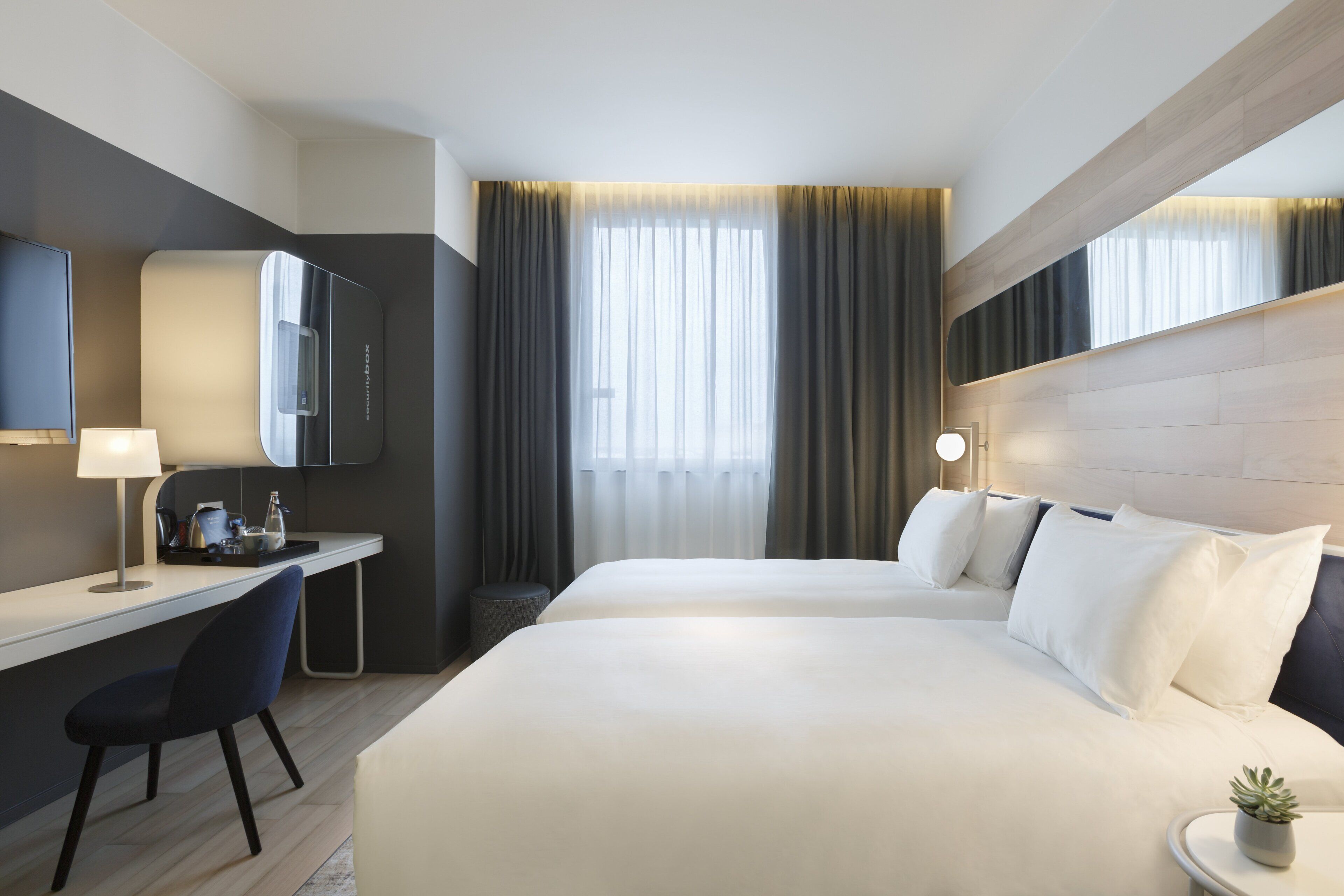 A hotel room with a bed, a desk, a chair, a TV, and a window with curtains.