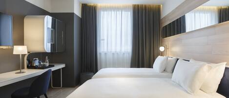 A hotel room with a bed, a desk, a chair, a TV, and a window with curtains.