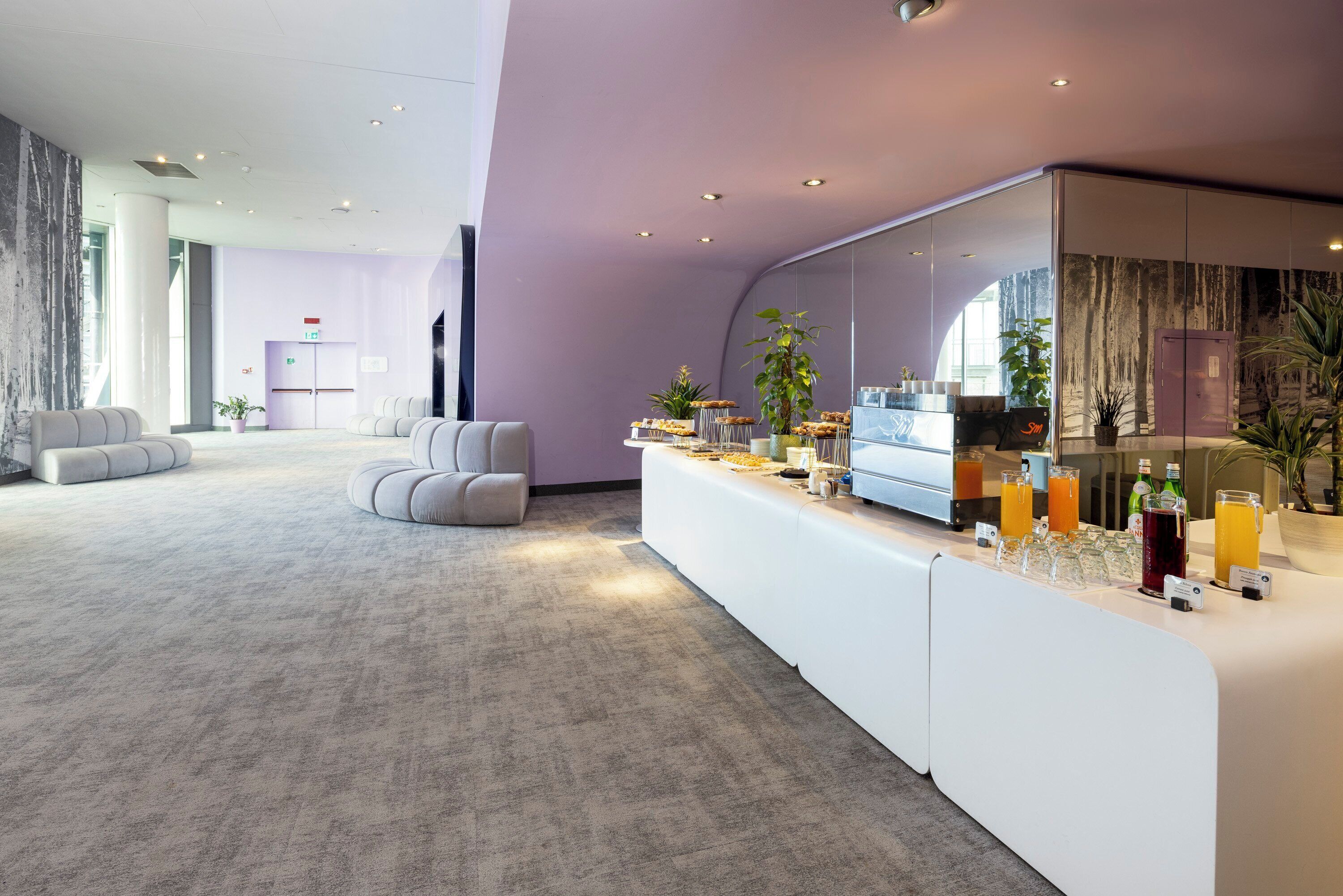 Een moderne hotelentree met een receptiebalie, zithoek en grote ramen.