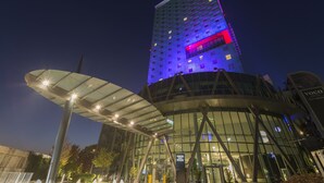 A modern building with a glass facade and a prominent vertical structure with illuminated signage.