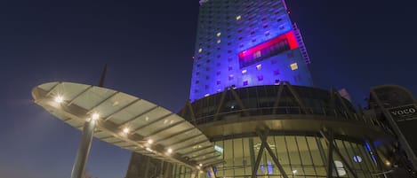 A modern building with a glass facade and a prominent vertical structure with illuminated signage.