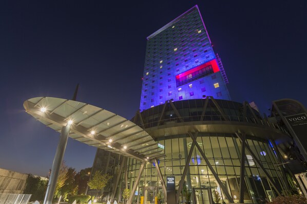 A modern building with a glass facade and a prominent vertical structure with illuminated signage.