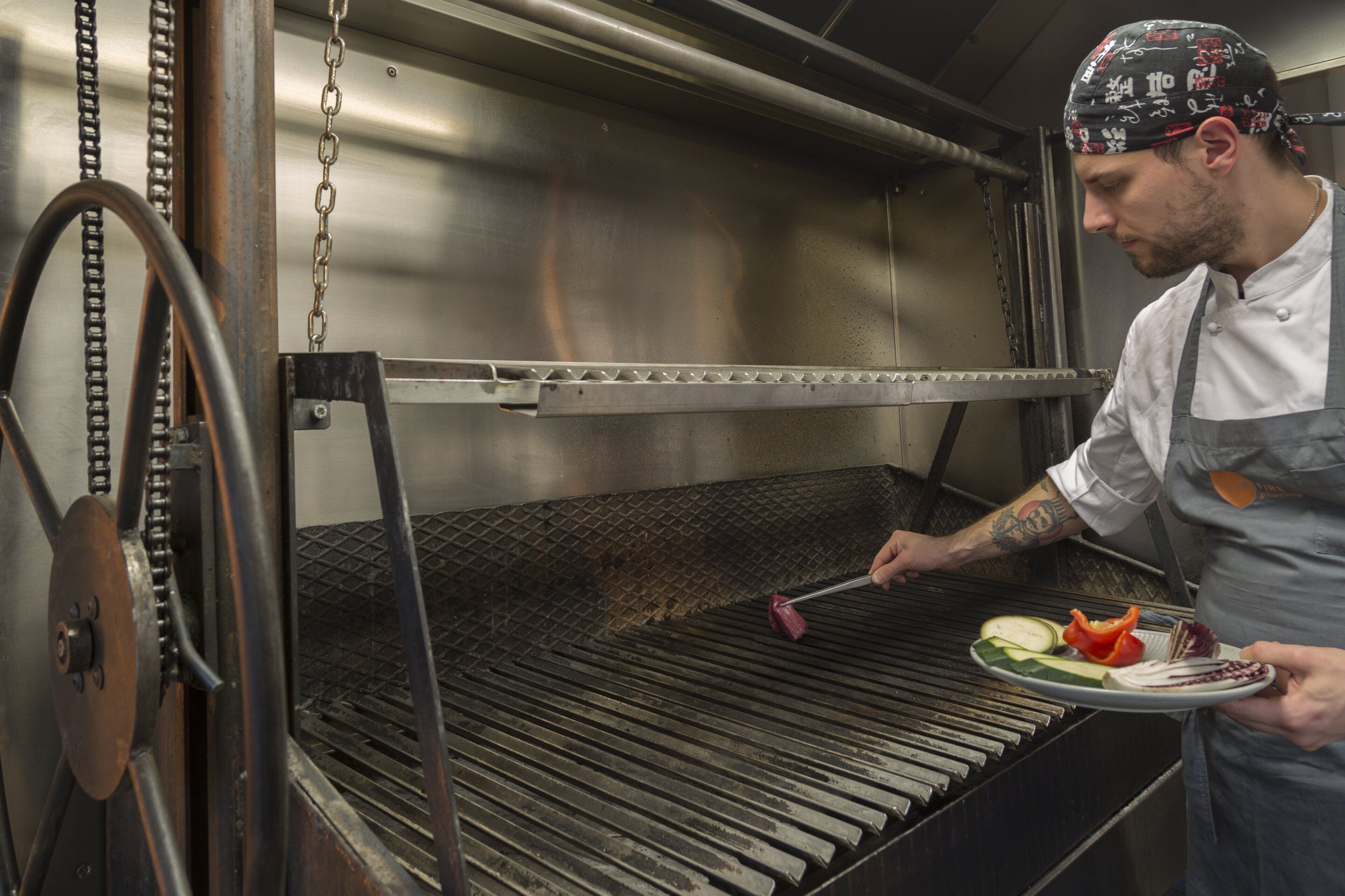 Um chefe de cozinha em uma cozinha profissional, com superfícies de aço inoxidável e um sistema de esteira transportadora.