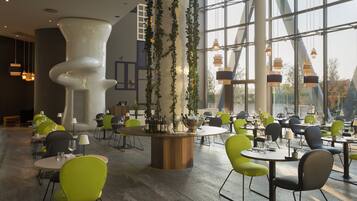 Un espace repas moderne avec des tables et des chaises rondes, un bar central où sont exposées des bouteilles, et de grandes fenêtres qui laissent entrer la lumière naturelle.