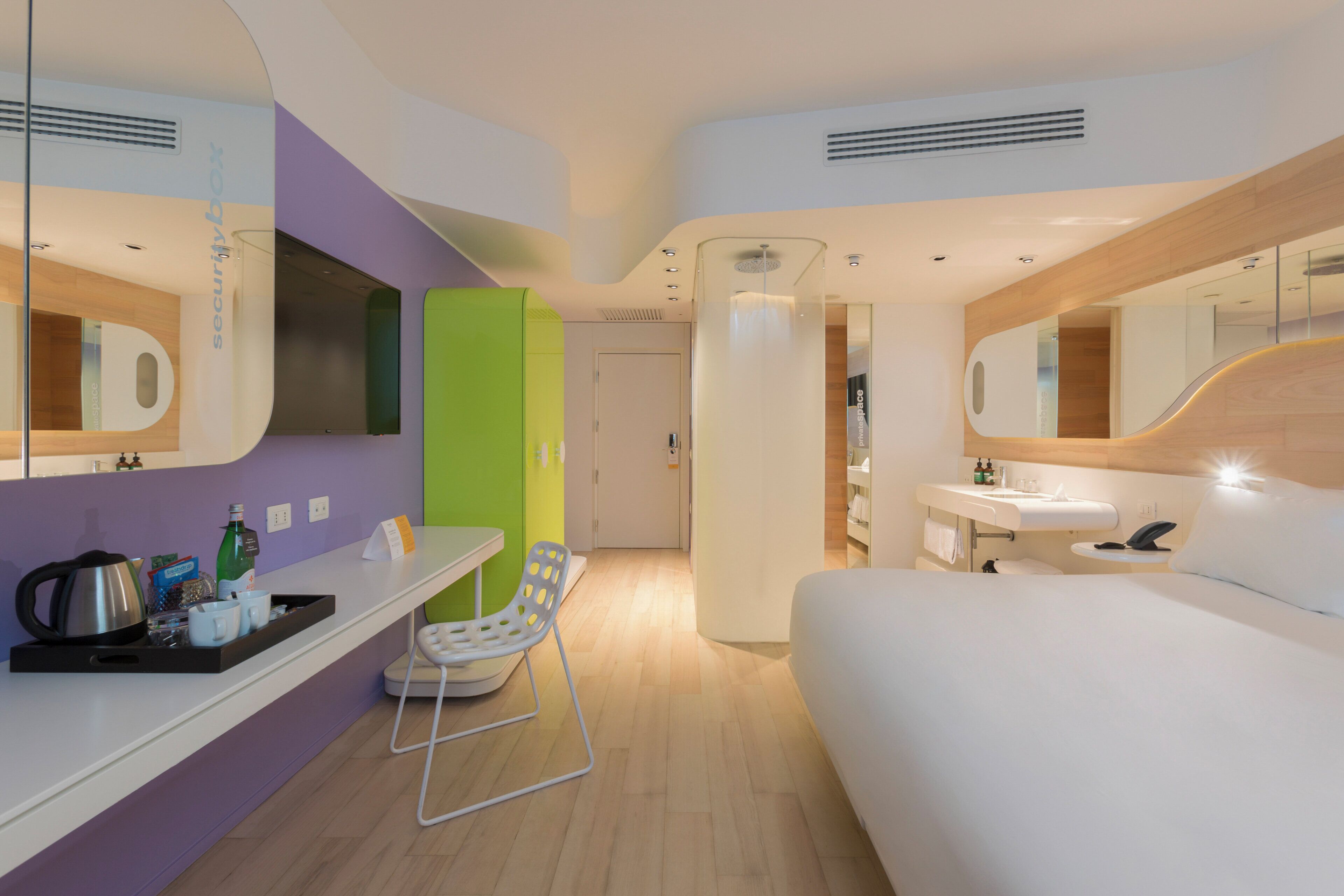 Une chambre d’hôtel moderne équipée d’un lit, d’un bureau, d’une chaise, d’une salle de bain et d’un miroir.