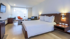 Une chambre d’hôtel avec un grand lit, un bureau avec une chaise, un canapé et un téléviseur fixé au mur.