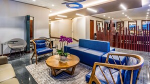 A modern lobby with a blue sofa, wooden chairs, a round wooden table, and a decorative ceiling. - NH Bogotá Urban 93 Royal (Bogotá)