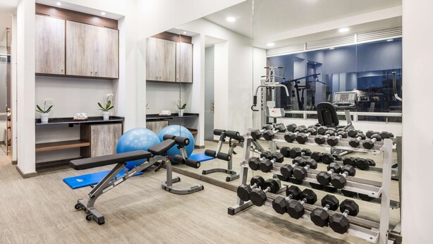 Une salle de sport moderne équipée de machines d’exercice, d’un banc et d’un porte-haltères.