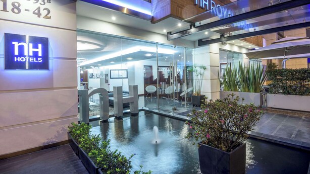 The exterior of NH Hotels with a modern glass facade, a water feature in front, and outdoor seating area. - NH Bogotá Urban 93 Royal (Bogotá)