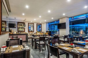 Un restaurante moderno con zona de bar, varias mesas para comer y vistas de la ciudad de noche.