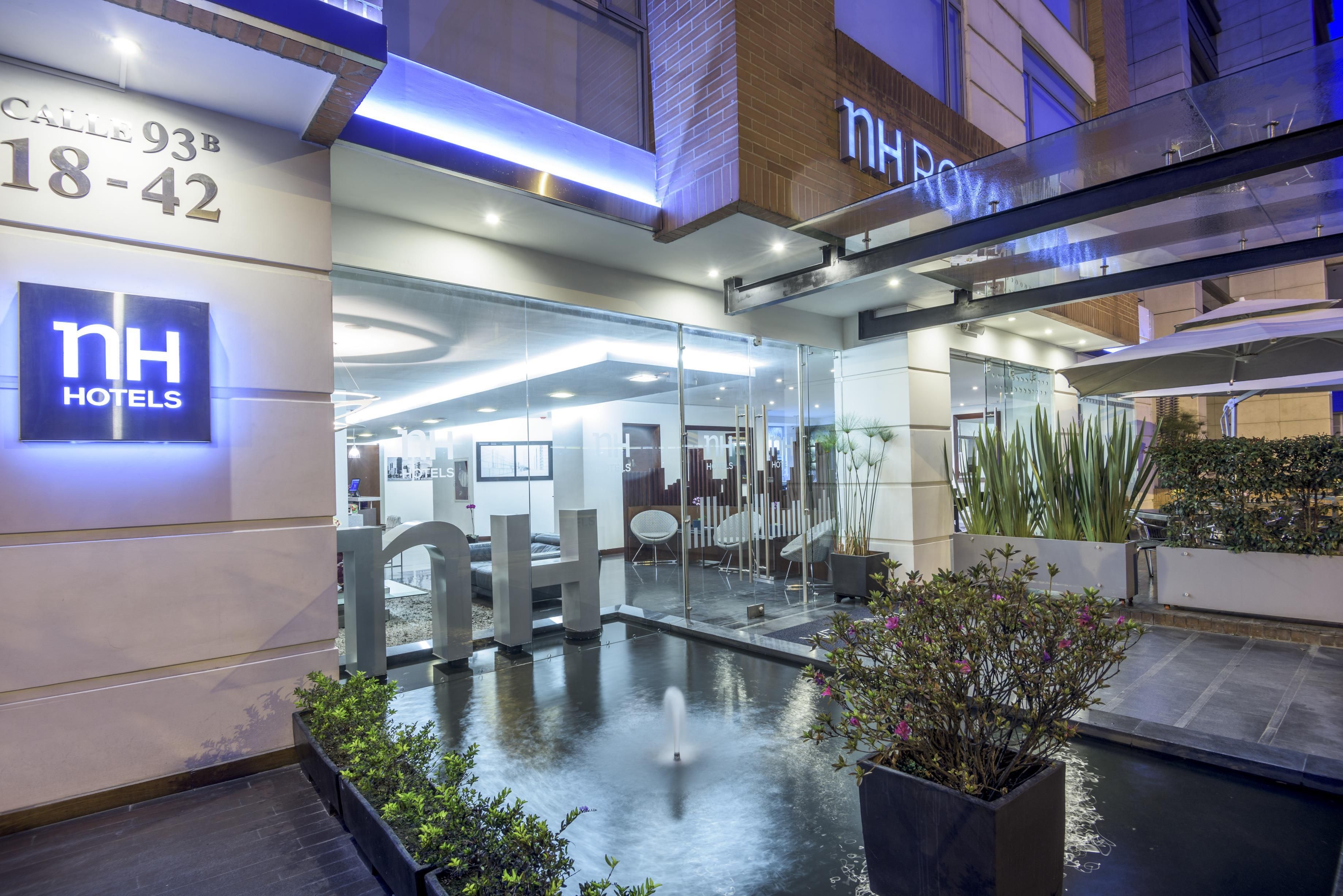 A hotel entrance with a glass facade, a reception desk, and a water feature in the courtyard.