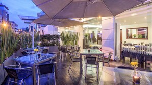 An outdoor patio area with glass tables and chairs, umbrellas, and potted plants. - NH Bogotá Urban 93 Royal (Bogotá)