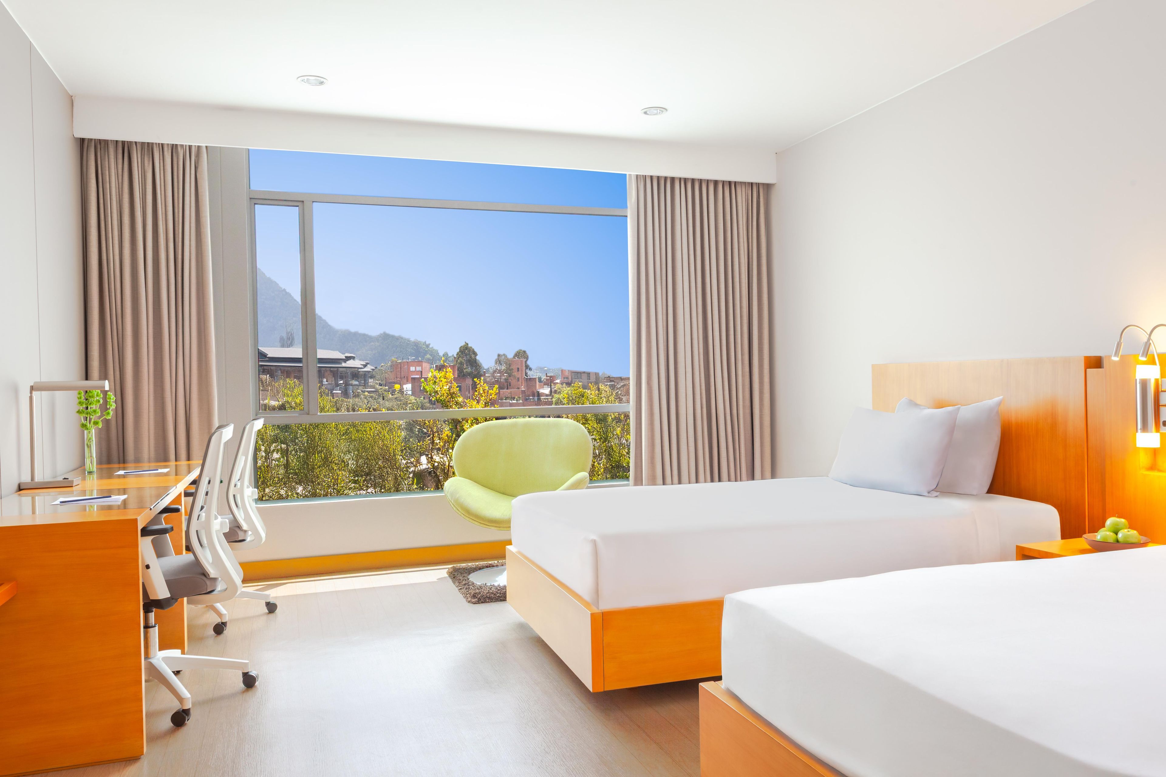 Ein Hotelzimmer mit großem Fenster, einem Bett, einem Schreibtisch und einem Sessel.