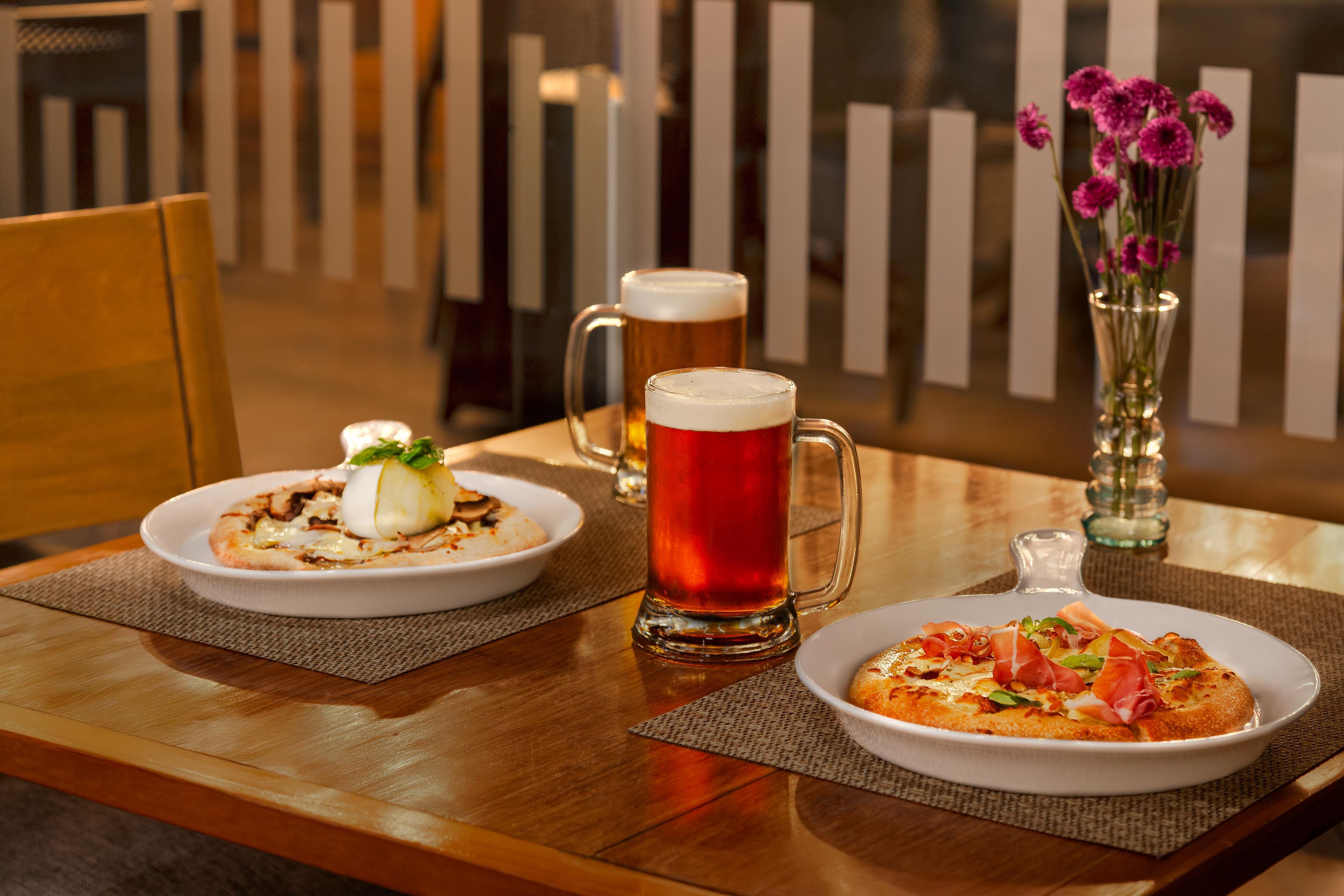 Une table à manger avec deux assiettes de nourriture, une chope de bière et un vase rempli de fleurs.