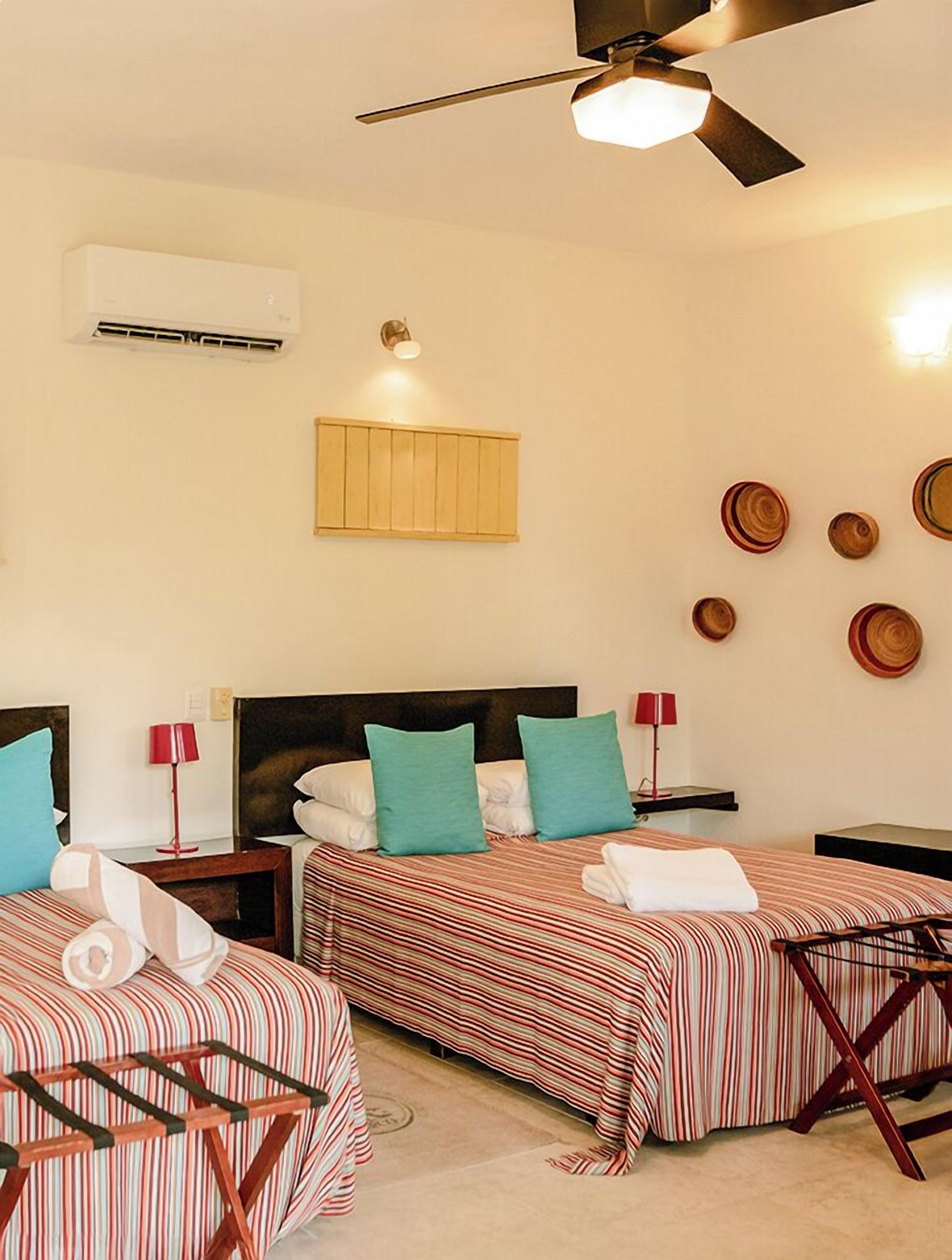 A hotel room with two beds, a ceiling fan, an air conditioning unit, and wall-mounted decorative plates.