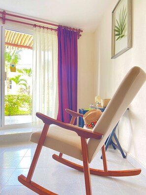 A rocking chair in a room with a view of greenery outside.