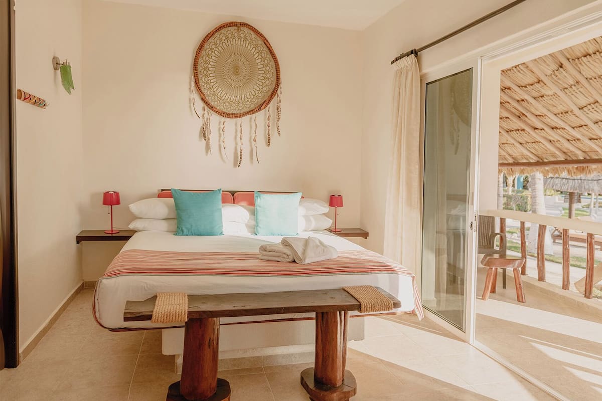 Un dormitorio con cama, mesitas de noche, un atrapasueños y vistas al balcón exterior.