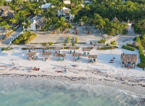 A beach resort with thatched-roof huts, palm trees, and a clear view of the ocean. - Hotel Puerto Holbox Beach Front (Isla Holbox)