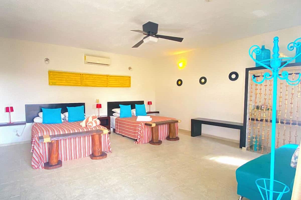 Una habitación amplia con dos camas, un ventilador de techo y un adorno en la pared.