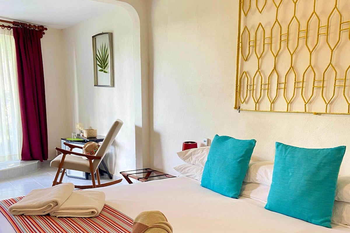 Habitación de hotel con cama, colcha a rayas, dos almohadas, una silla, una mesa y un adorno de pared.