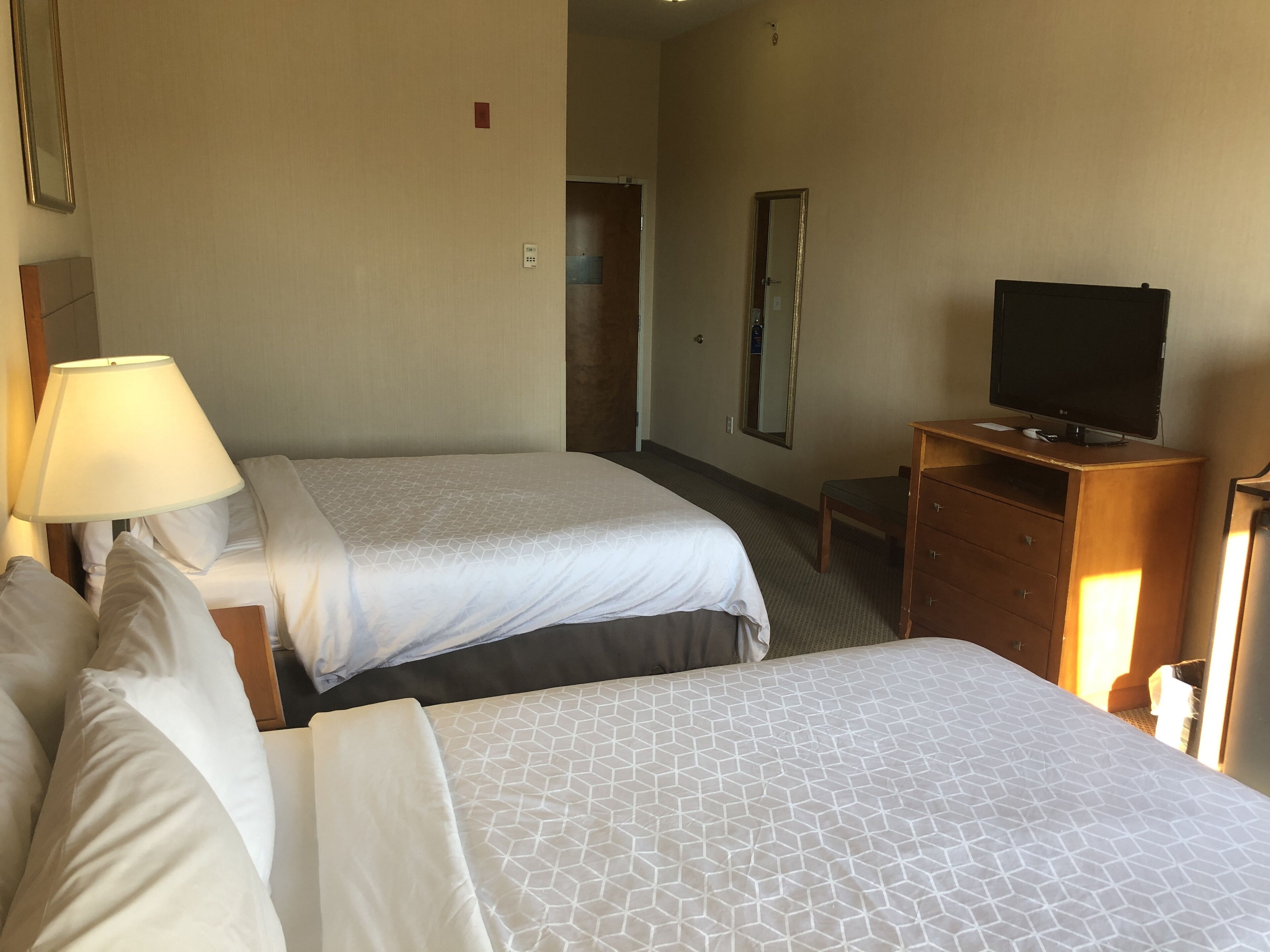 A hotel room with two beds, a TV on a wooden stand, and a lamp on the left side.