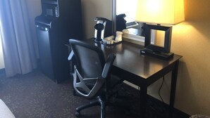 A hotel room with a desk, a chair, a coffee machine, a phone, and a window with curtains.