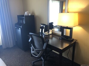 Hotelkamer met bureau, stoel, koffieapparaat, telefoon en raam met gordijnen.